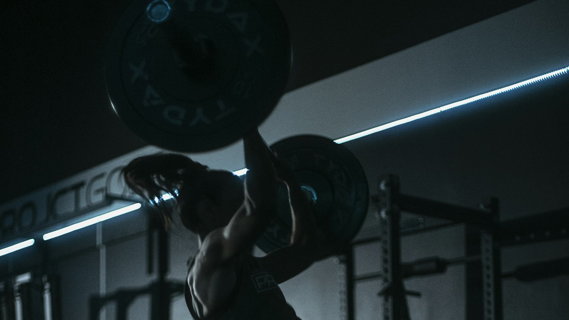 Athlete pressing a barbell overhead in a dark gym